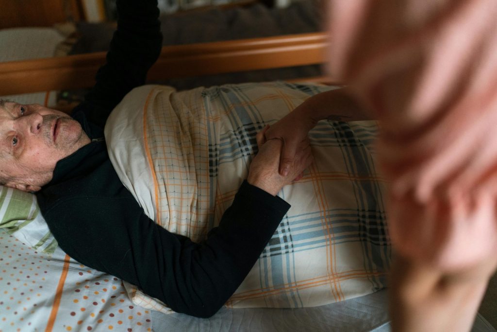 A caregiver holding hands with a senior adult, providing support and reassurance at home.